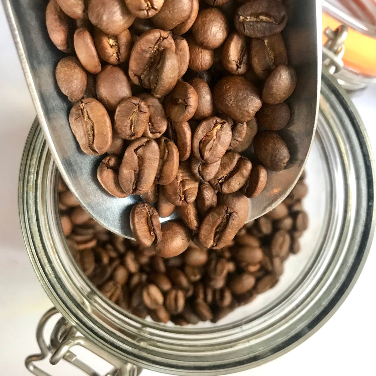 Coffee beans in metal scoop flowing into a glass jar