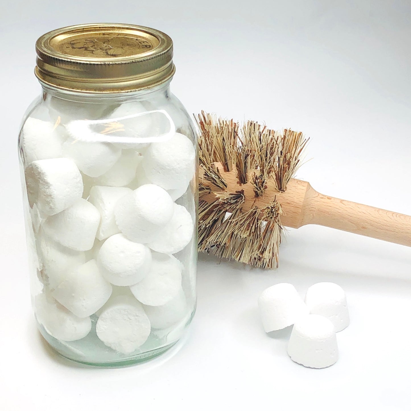 White toilet bombs in a glass jar with a wooden toilet brush with natural bristles along side 3 toilet bombs all on a white background