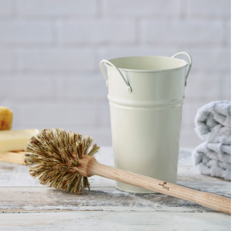 Wooden toilet brush with natural bristles on a wooden table with a cream coloured metal holder in the mid ground