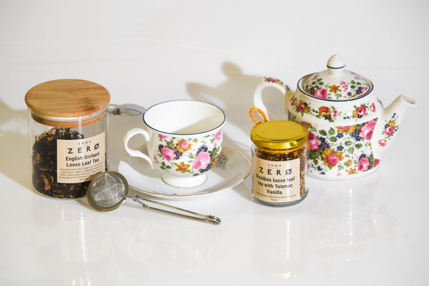 Glass containers containing loose leaf and a tea infuser from Shop Zero with a cup and saucer and tea pot
