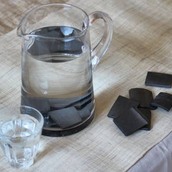 Clear pitcher with water and dark chocolate pieces on a wooden surface