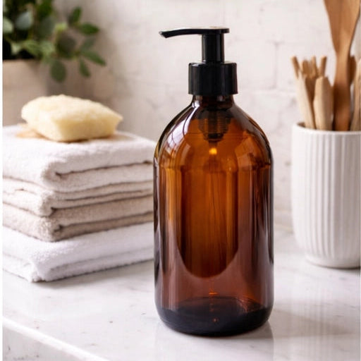 500ml amber glass bottle with a pump in front of a stack of white and beige towels.