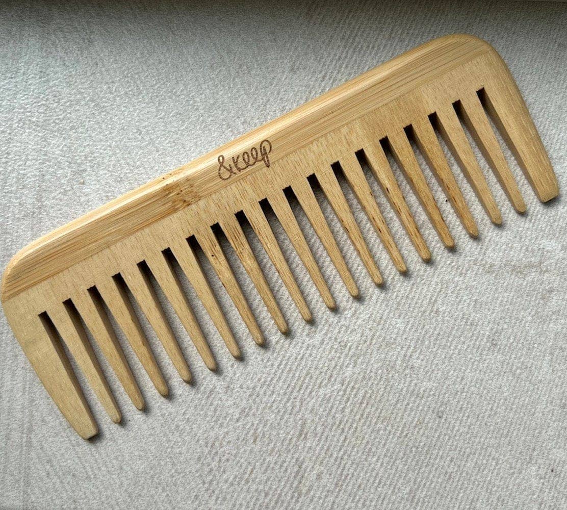 Wooden wide tooth comb with '&keep' branding pictured on a textured gray background