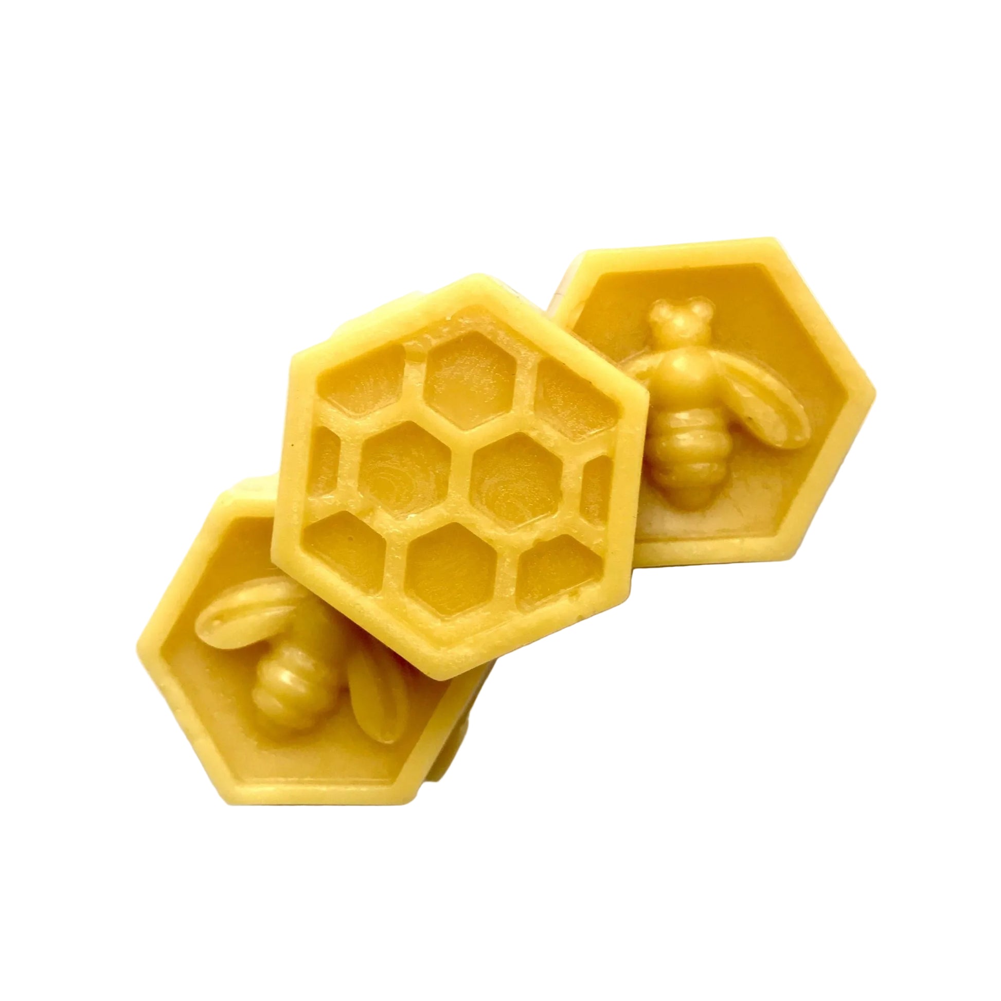 Three small yellow hexagonal beeswax blocks arranged on a white surface, including one block with a honeycomb pattern and two with raised bee designs.