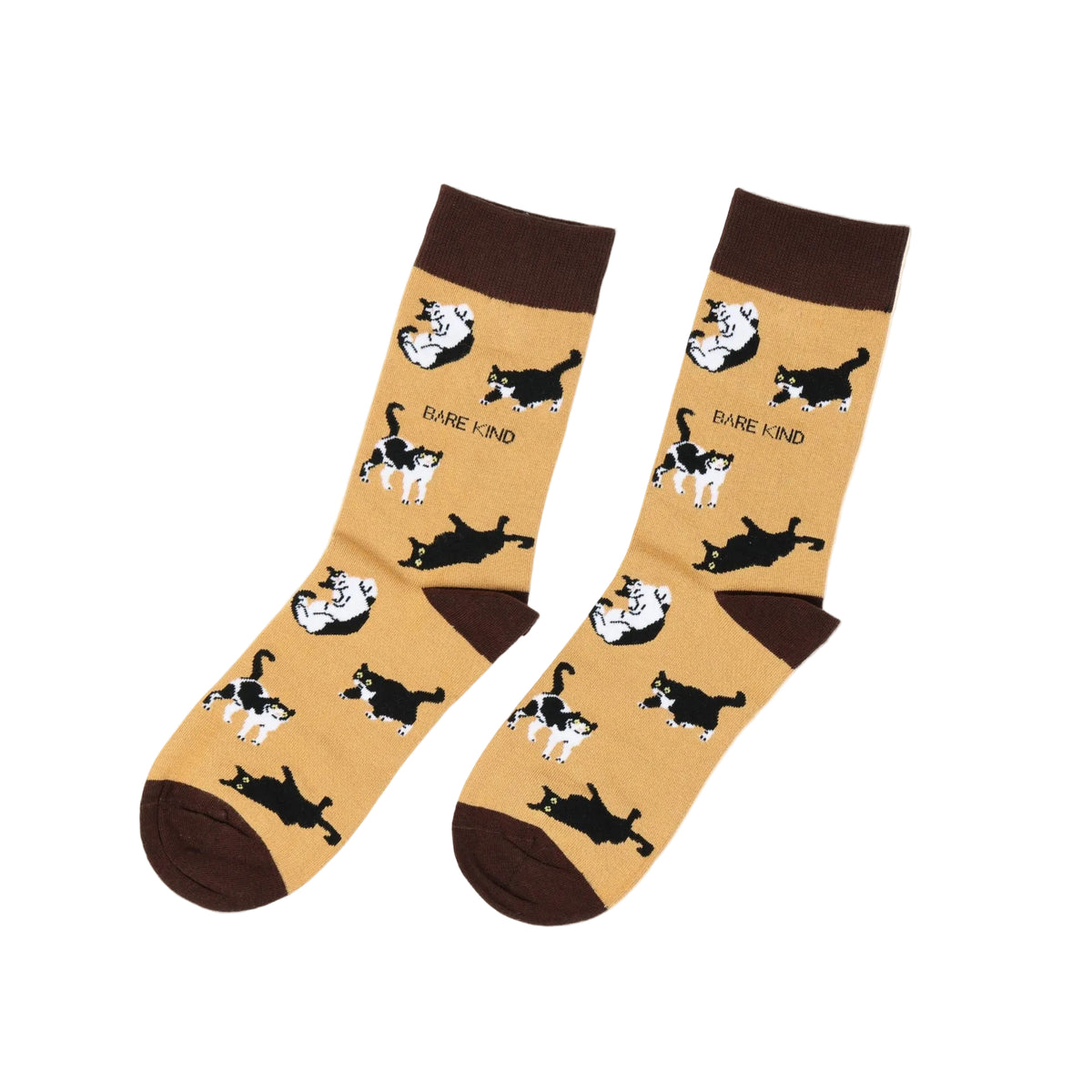 A pair of beige crew socks with a pattern of black and white cats lying down and dark brown cuffs, heels, and toes. The word 'DARE KIND' is printed in black near some of the cat illustrations.