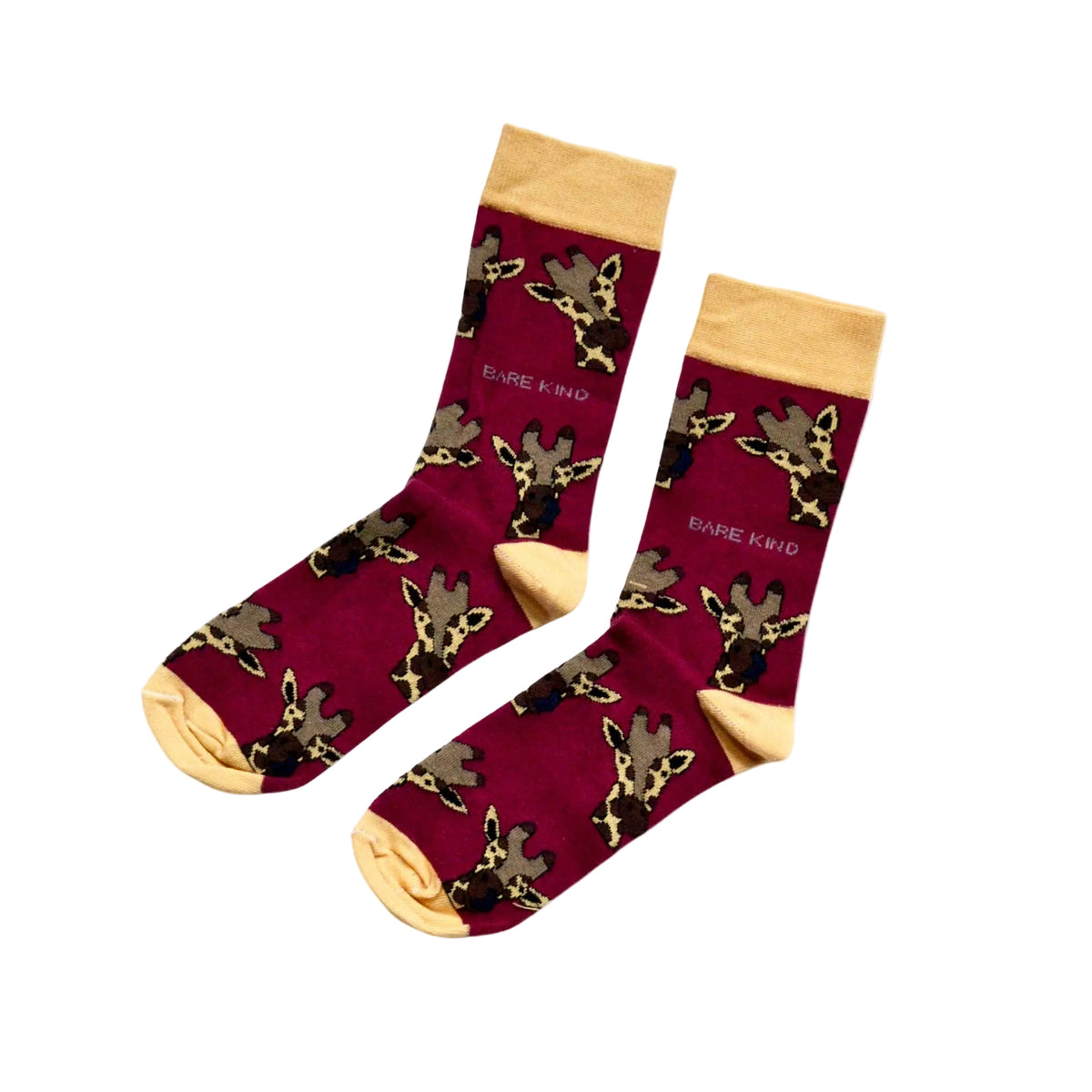 A pair of crew socks with a deep burgundy background patterned with cartoon giraffes in black, beige, and brown, featuring light beige cuffs, heels, and toes. The brand name 'BARE KIND' is printed in white near the upper leg.
