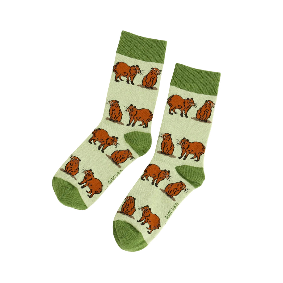 A pair of crew socks with a repeating pattern of orange-brown capybara illustrations on a pale cream background, featuring solid green cuffs, heels, and toes, displayed against a pale yellow background.