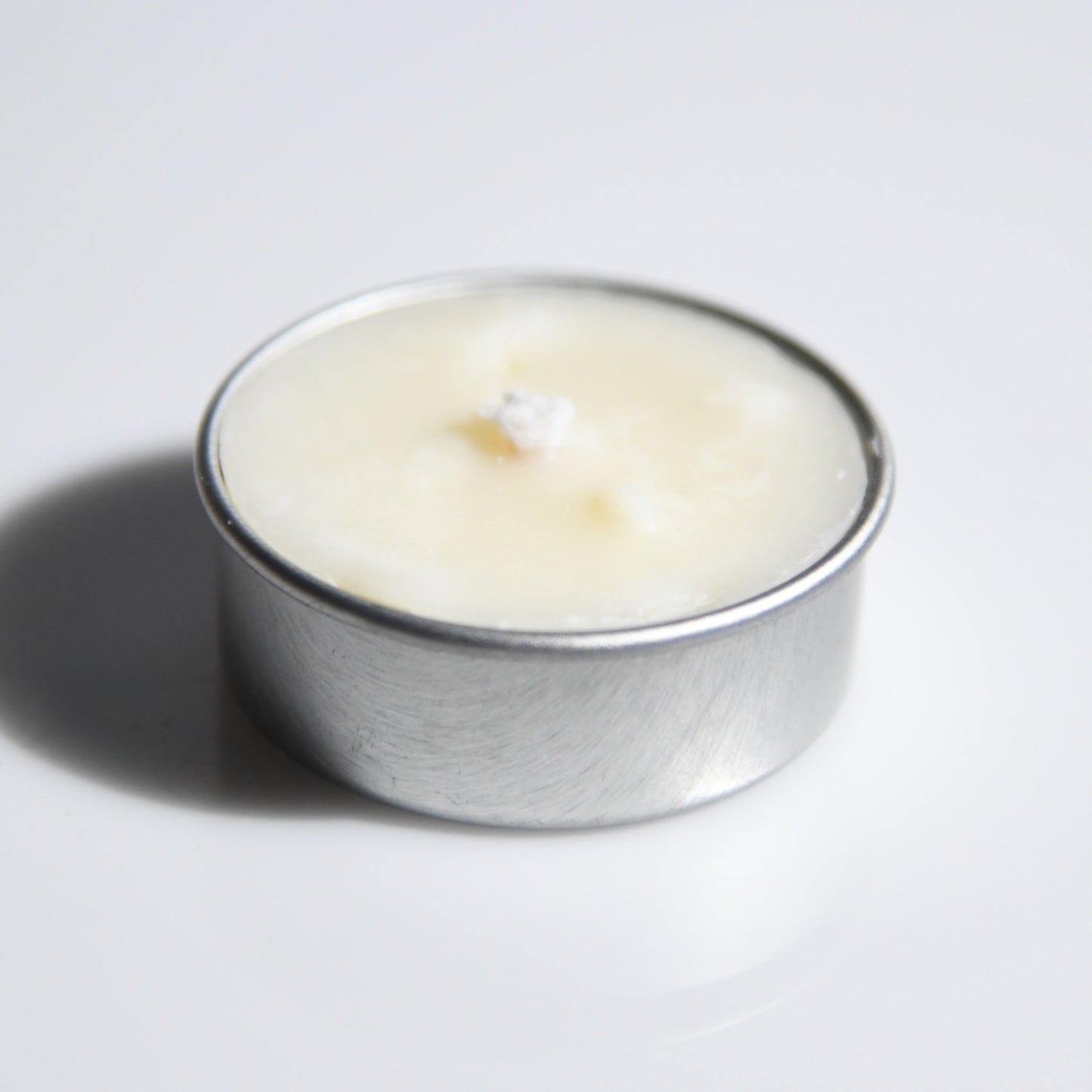 A small silver metal tealight candle with creamy off-white wax, photographed on a plain light gray background with a soft shadow.