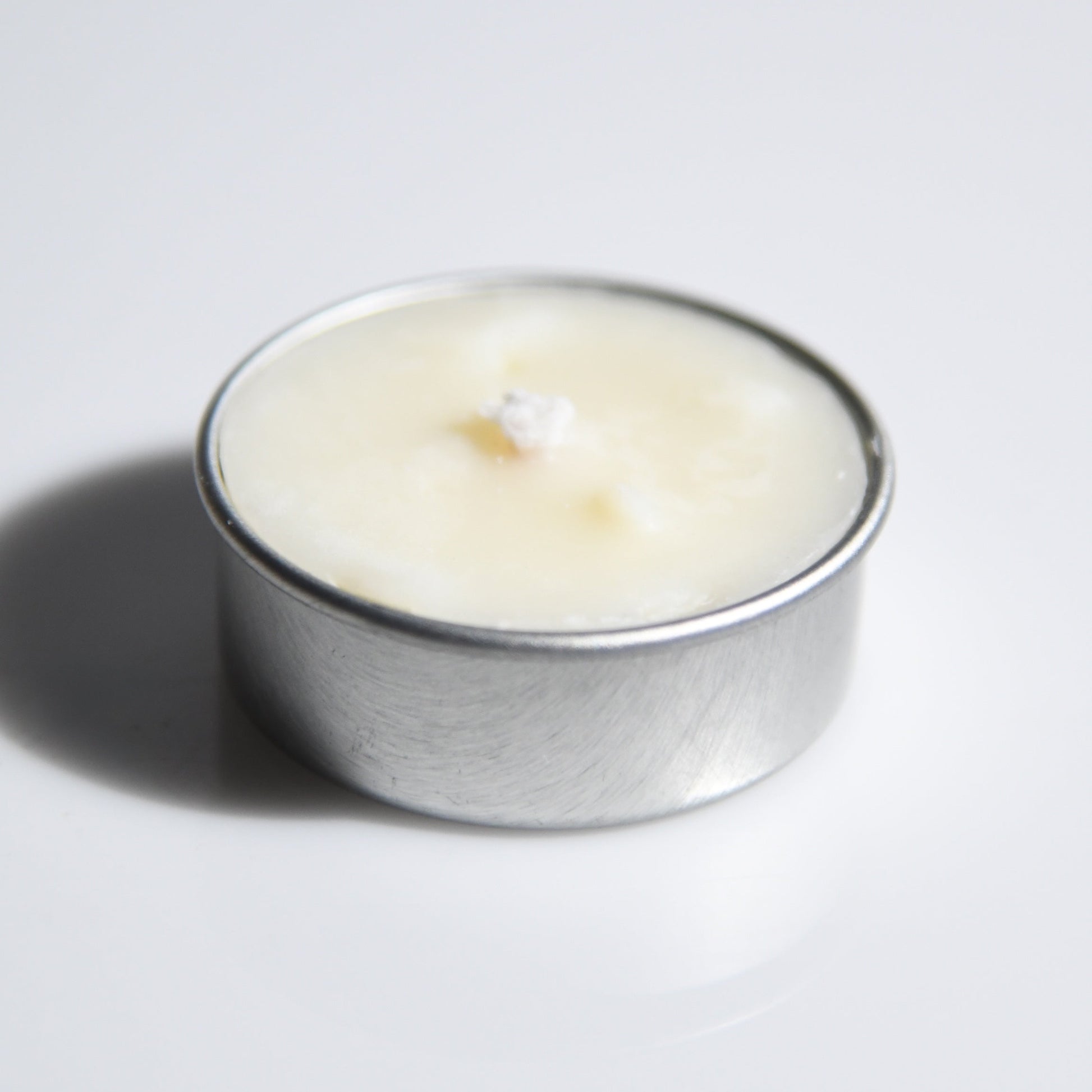 A small silver metal tealight candle with creamy off-white wax, photographed on a plain light gray background with a soft shadow.