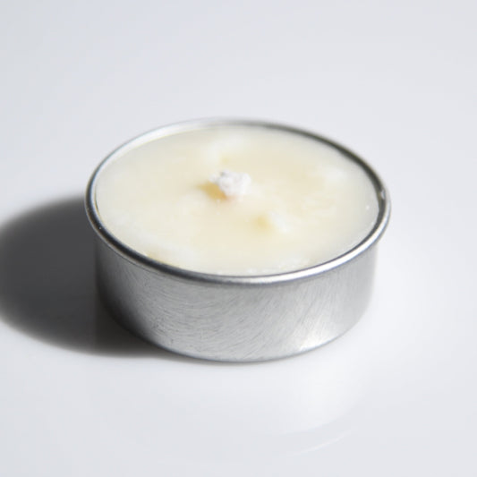 A small silver metal tealight candle with creamy off-white wax, photographed on a plain light gray background with a soft shadow.