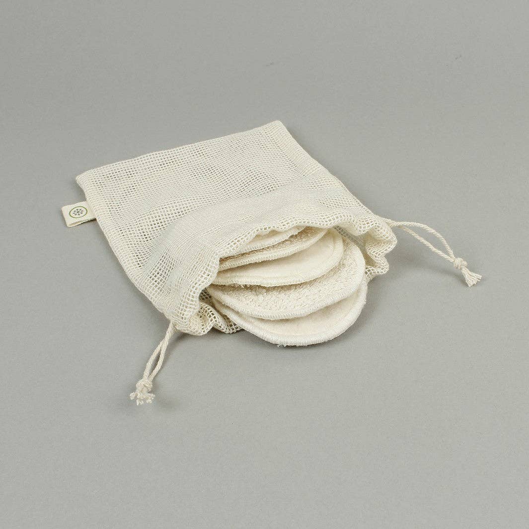 A set of off-white cotton mesh drawstring bags with round cotton make up pads inserted, photographed on a neutral gray background.