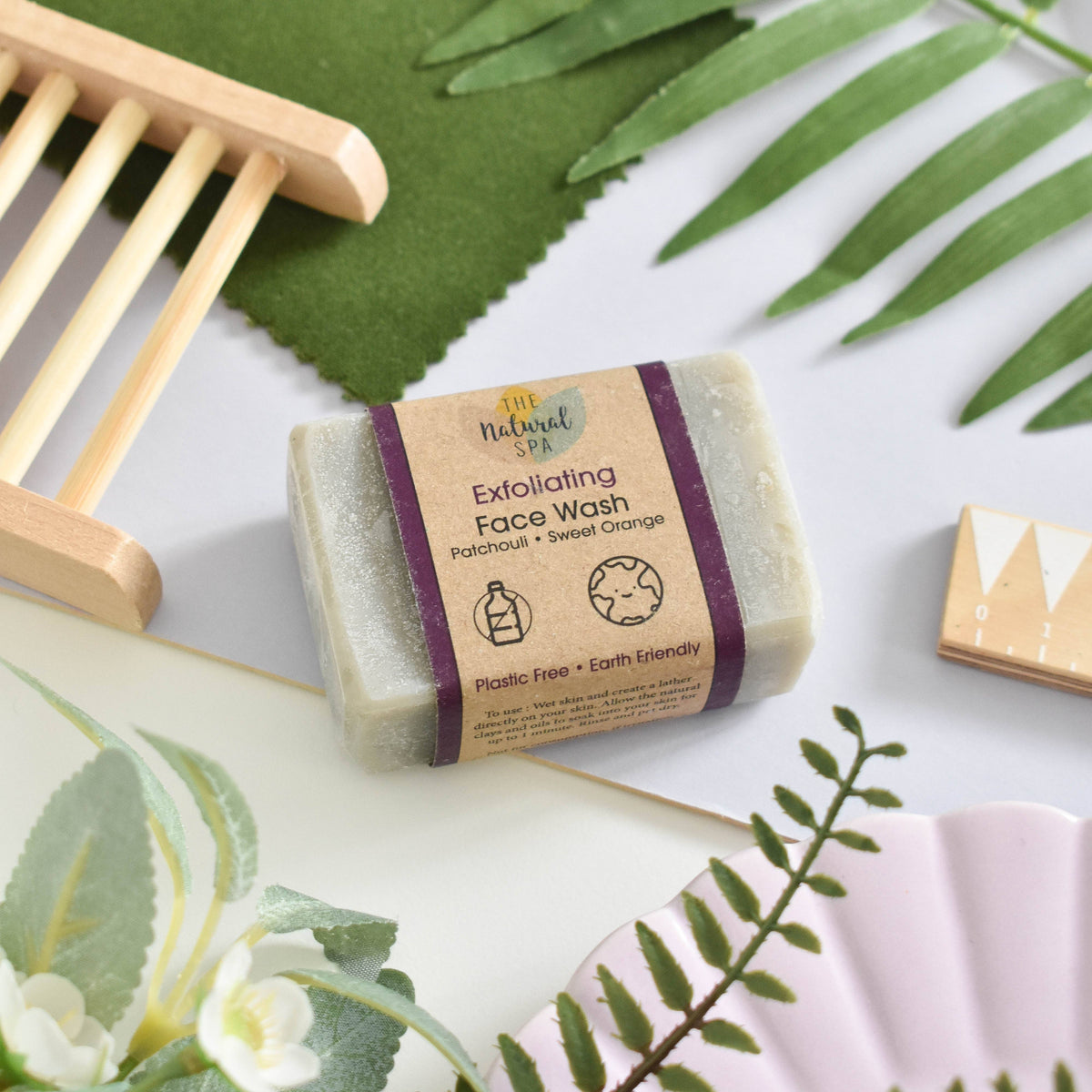 Bar of exfoliating face wash with a natural label on a white surface with green leaves.
