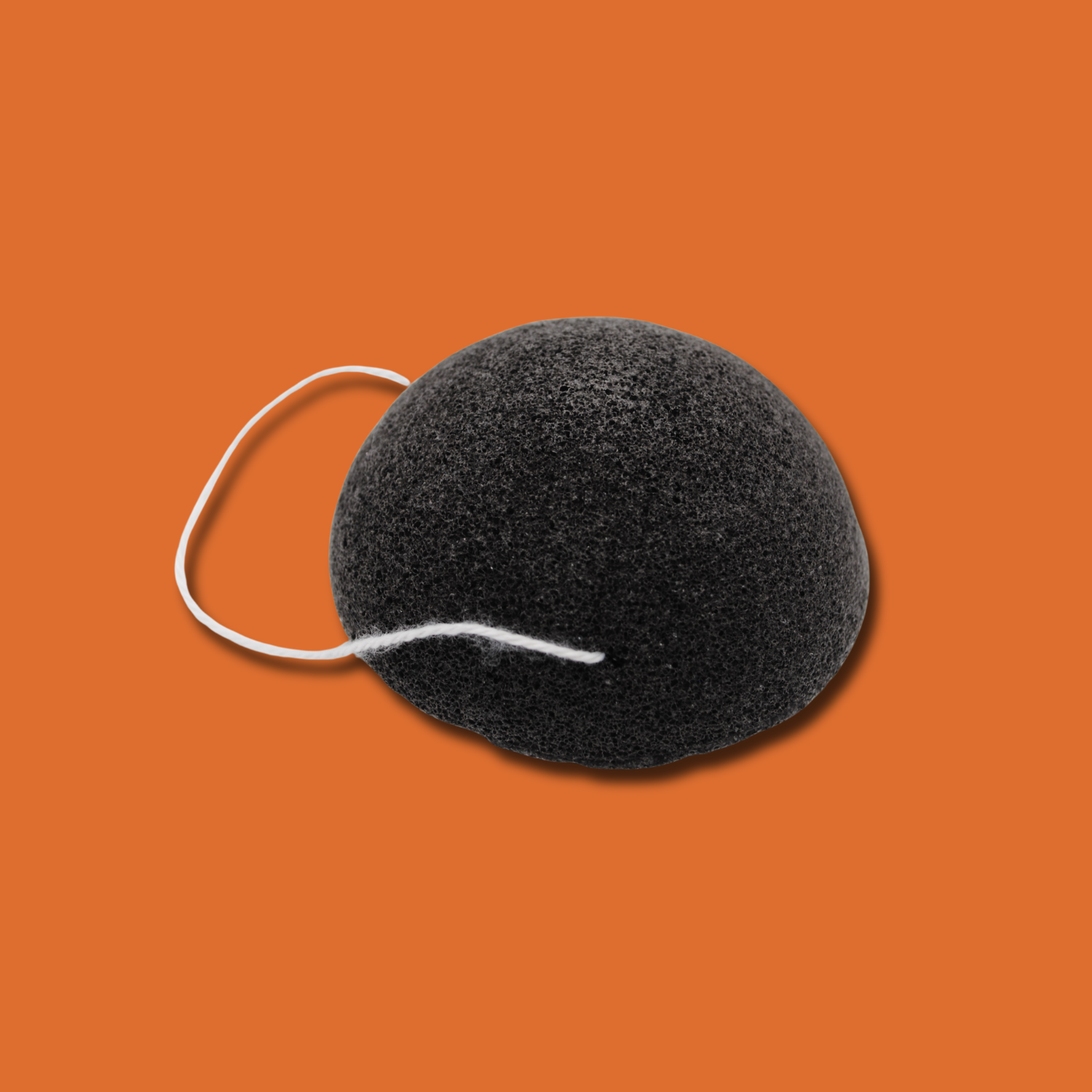 Activated charcoal, plastic free konjac sponge with a white string on an orange background