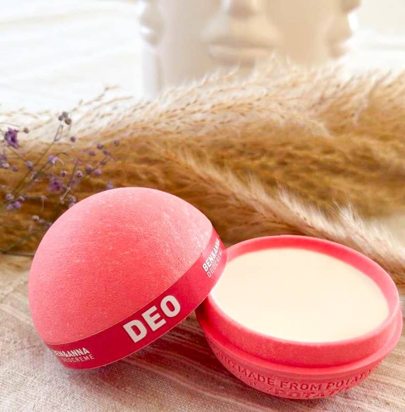 Pink deodorant container with white cream inside on a soft fabric background