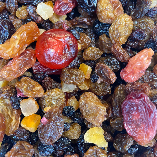 A close-up pile of mixed dried fruit, including dark and light brown raisins, a glossy red cranberry, and small yellow lemon and orange dried peel pieces.