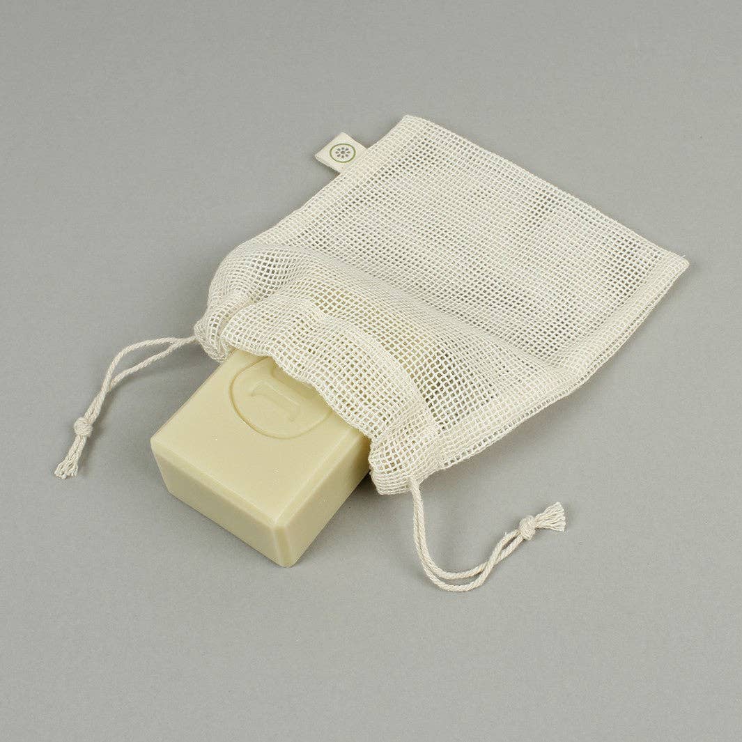 An off-white mesh drawstring soap bag containing a pale yellow bar of soap, photographed on a neutral gray background.