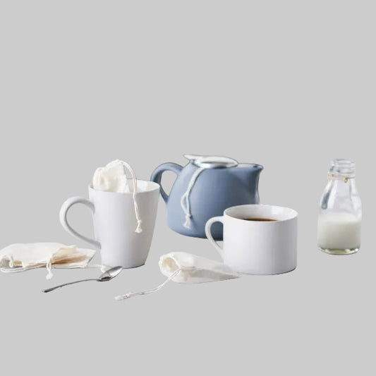 Two mugs with tea bags, a teapot, and a bottle of milk on a kitchen counter.