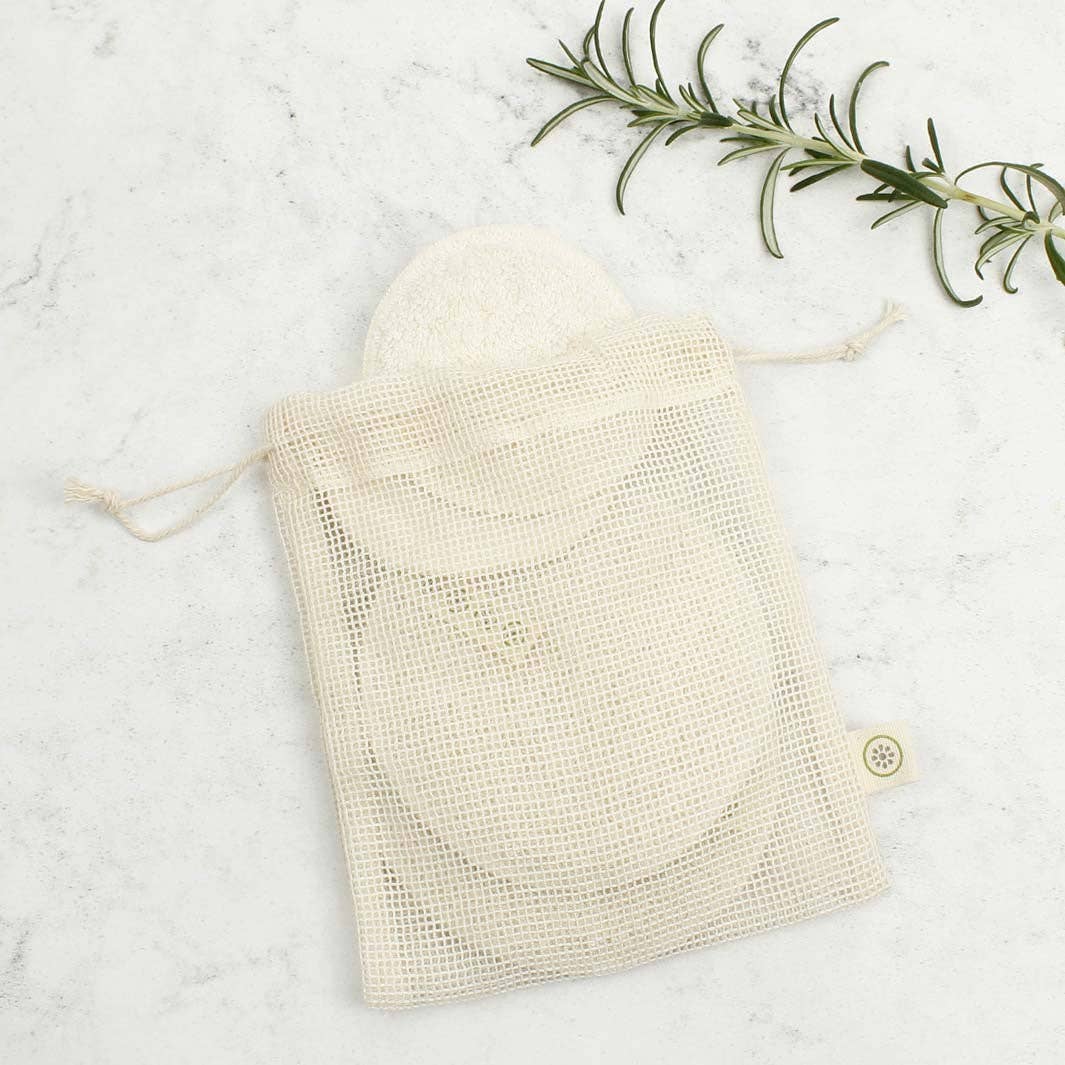 A mesh cotton storage bag containing reusable make up  pads show on a light background with a rosemary stalk