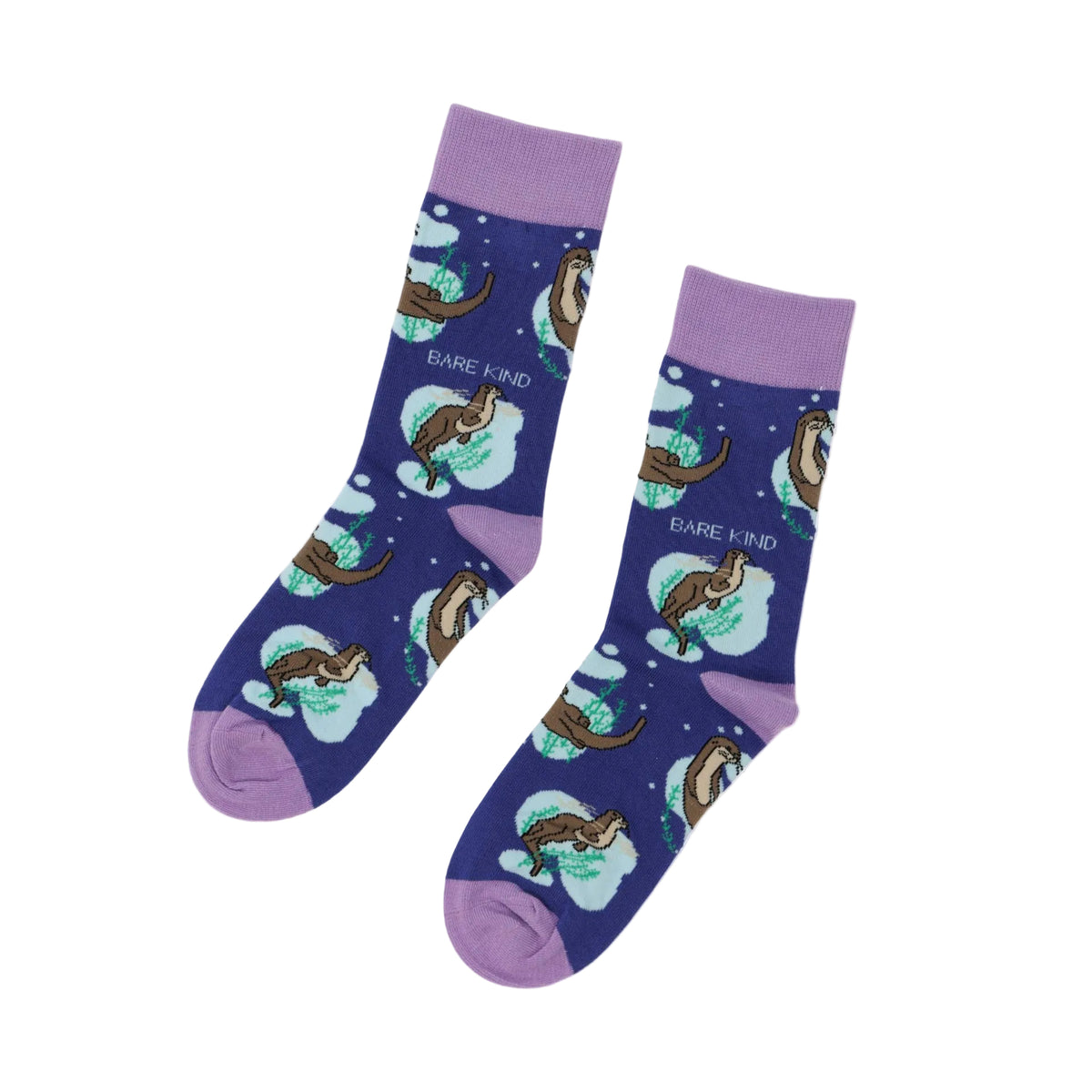 A pair of crew socks with a dark blue background featuring cartoon otters in snowy scenes and the text 'BARE KIND'. The socks have light purple cuffs, heels, and toes, and are displayed on a clean white background.