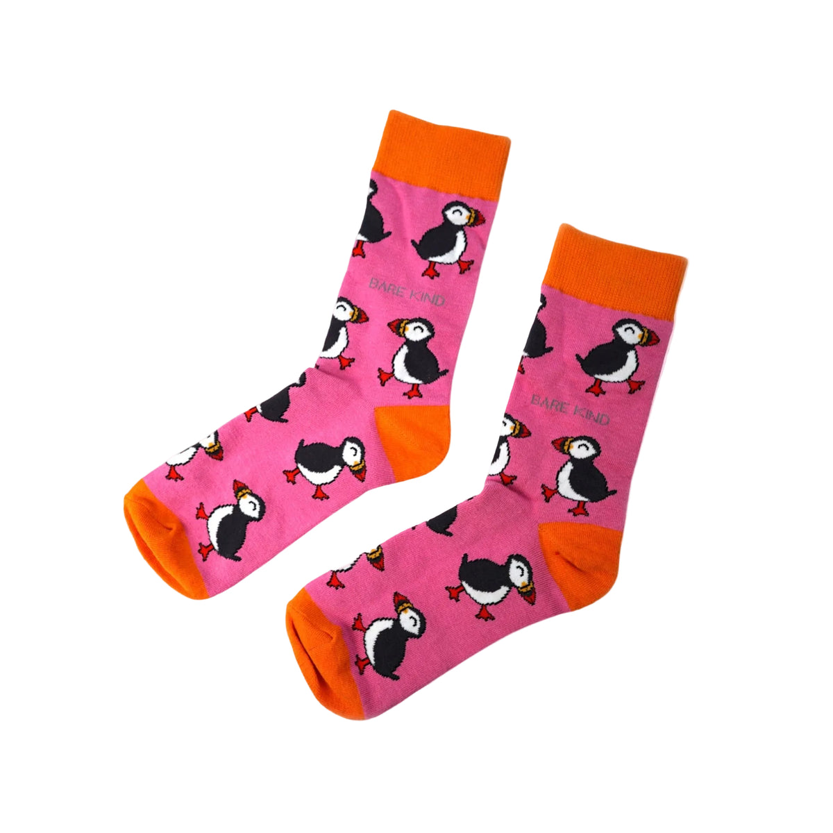 A pair of pink crew socks with an all-over puffin print, featuring bright orange cuffs, heels, and toes, displayed against a solid light pink background.