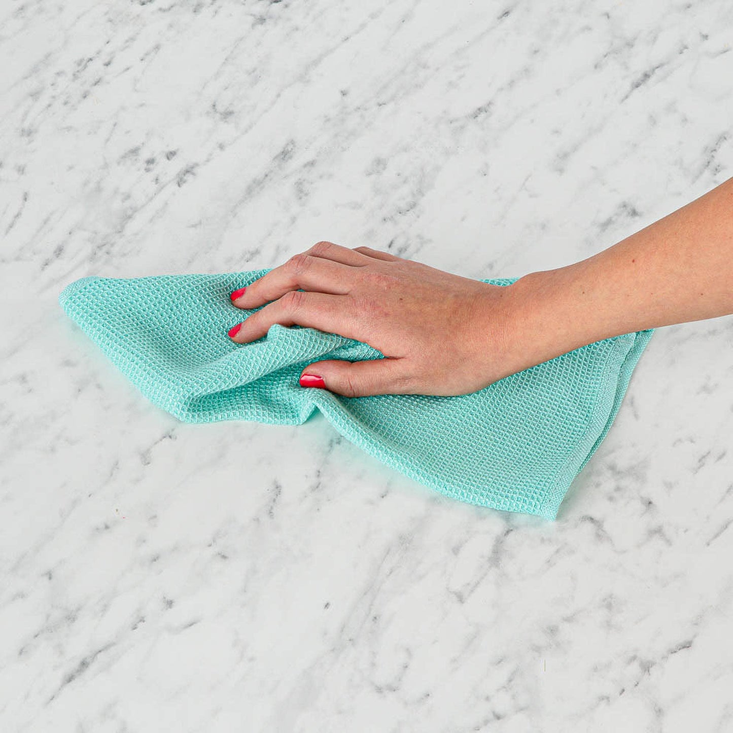 Hand holding a teal Seep bamboo cleaning cloth on a marble surface