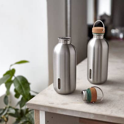 Two stainless steel water bottles with wooden caps on a table indoors.