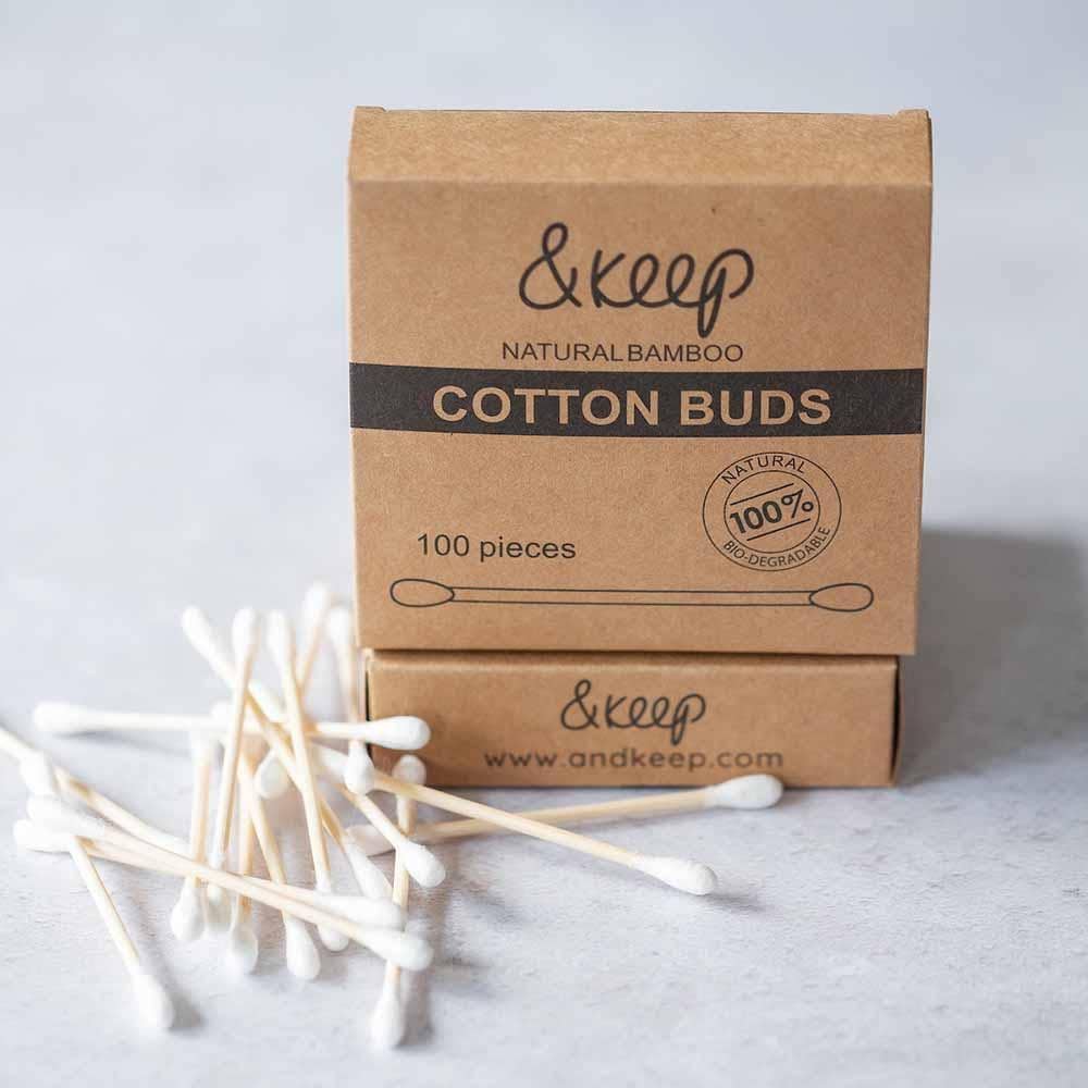 A kraft card box of ustainable bamboo cotton buds with some scattered by the box, all shown on a light grey background.
