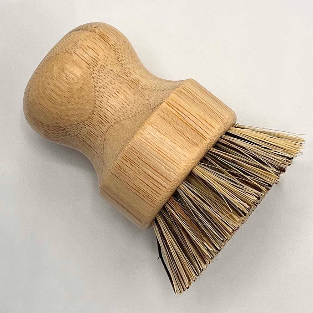 A small hand brush with a rounded natural wood handle and a wide band of natural straw-colored bristles, photographed on a plain light background.