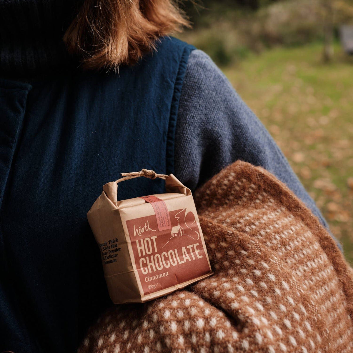 Person holding a small kraft bag of hot chocolate in a natural setting