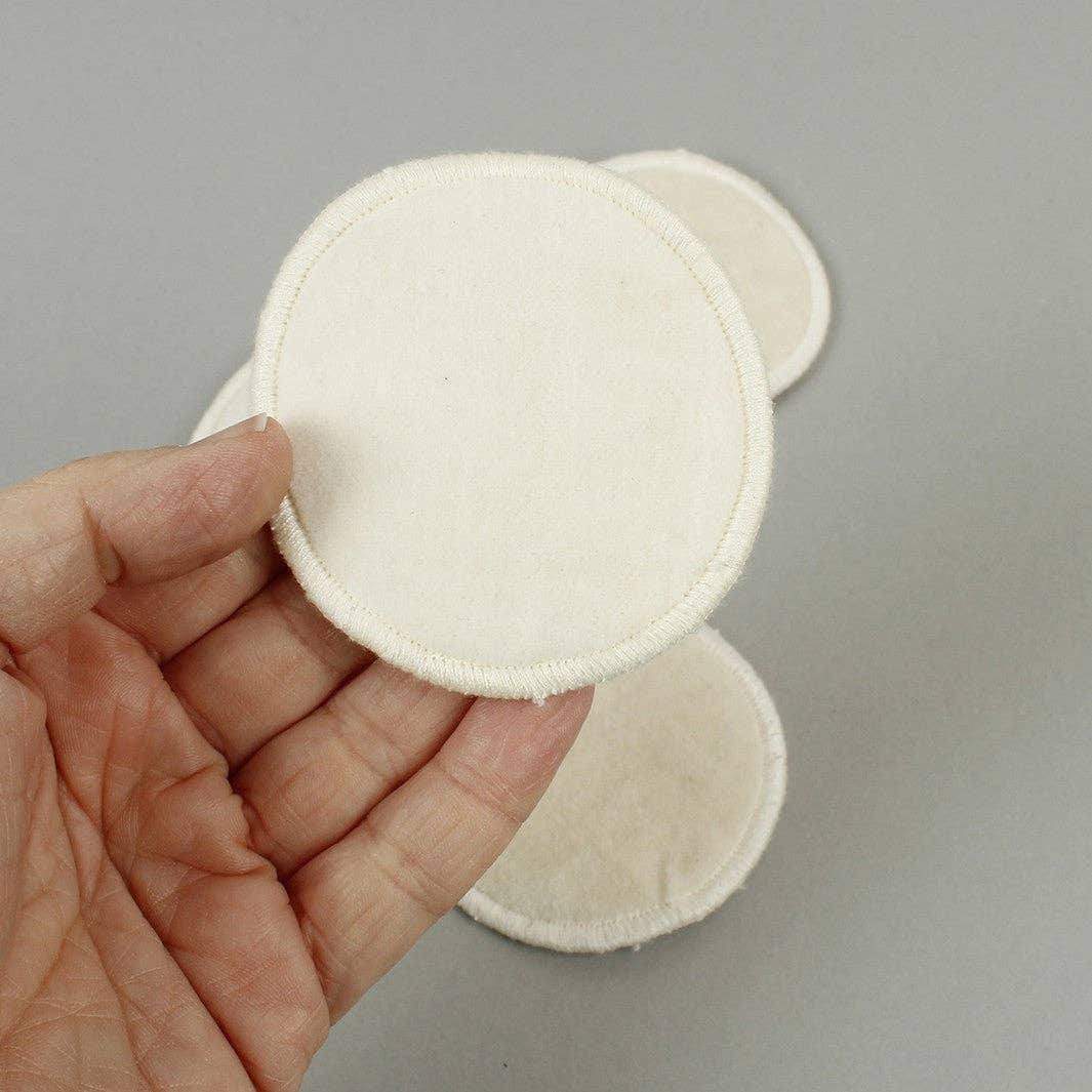 Organic cream  circular fabric make-up pad held in a person's hand against a gray background