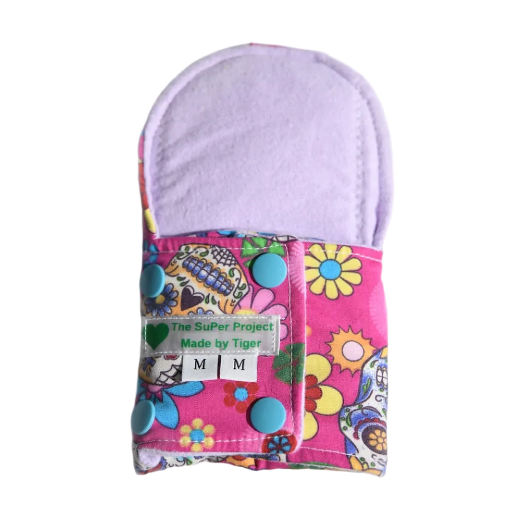 A washable period pad showing the lilac coloured brushed cotton inner, with a pink colouful skull cotton fabric outer on a white background.